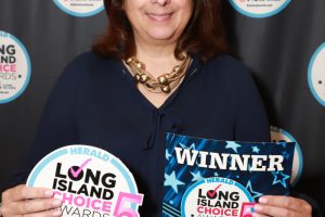Woman with brown hair in a navy blouse holding Long Island Choice Awards signs, smiling at the camera.
