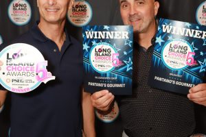 Two men smile at the camera, each holding Long Island Choice Awards winner items in front of a branded backdrop. One holds a round award plate, the other holds two blue winner plaques for Pantano's Gourmet.