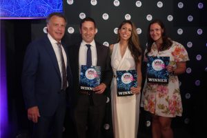 Four people pose on a dark backdrop at an awards event, each holding a blue 'WINNER' certificate for the Long Island Choice Awards with circular logos in the background.