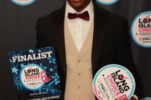 Man in a suit posing at the awards backdrop, holding a finalist plaque and a circular Long Island Choice Awards sign.
