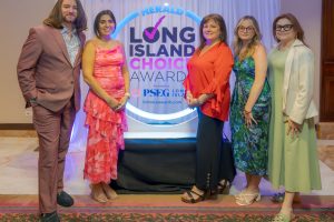 Six adults pose for a photo on a stage in front of a glowing 'Herald Long Island Choice Awards' backdrop, smiling at the camera.
