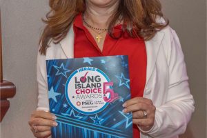 Smiling woman in a red blouse and white blazer holds a blue 'Winner' card for the Long Island Choice Awards.