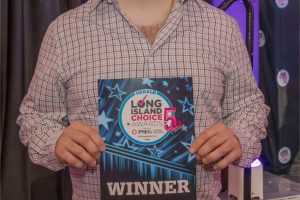 Bearded man in a plaid shirt holds a blue 'WINNER' award plaque at the Long Island Choice Awards stage.