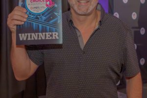 Smiling man with a shaved head holds a blue award plaque that reads 'Long Island Choice Awards' and 'WINNER.'