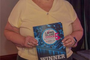 Smiling woman in a pale yellow sweater holds a blue 'WINNER' plaque at the Long Island Choice Awards.