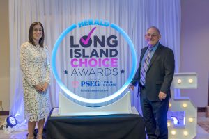 Two well-dressed individuals stand beside a circular illuminated sign reading 'Long Island Choice Awards' at a ceremony backdrop.