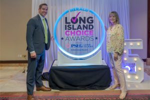 Two people in business attire pose beside a glowing circular sign that reads 'Long Island Choice Awards' at an event backdrop.