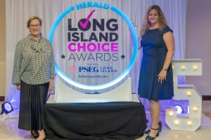 Two women pose beside a glowing circular sign that reads Herald Long Island Choice Awards, with the PSEG Long Island logo nearby.