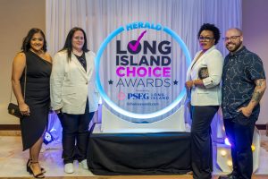 Four people pose for a photo beside a circular neon sign that reads Herald Long Island Choice Awards, at a ceremony backdrop.