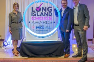 Three well-dressed people pose with a glowing circular 'Long Island Choice Awards' sign at an event.