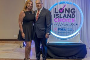 Couple posing together at the Herald Long Island Choice Awards, with a circular neon sign behind them.
