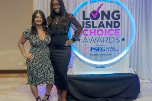 Two women in cocktail attire pose and smile beside a glowing circular sign for the Long Island Choice Awards.