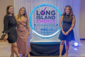 Three women in dresses pose together in front of a blue-lit Long Island Choice Awards backdrop.