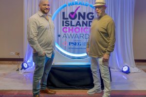 Two men pose for a photo in front of a Long Island Choice Awards backdrop with a circular neon design.