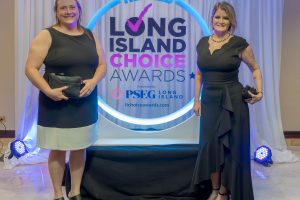 Two women in black dresses pose for a photo at the Long Island Choice Awards backdrop with a blue circular LED ring behind them in a formal setting.