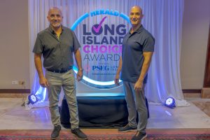 Two men pose for a photo in front of a circular illuminated backdrop that reads Herald Long Island Choice Awards.