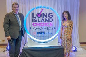 Two people pose beside a glowing circular display that reads 'Long Island Choice Awards' with Herald branding in the background behind a white curtain.