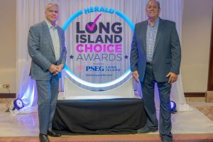 Two men in business suits pose on either side of a glowing circular sign reading 'Long Island Choice Awards' at a staged event backdrop.