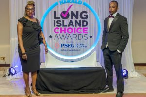 Two formally dressed individuals pose beside a circular neon-lit sign reading 'Herald Long Island Choice Awards' at a staged backdrop.