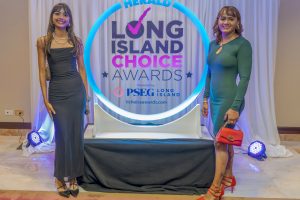 Two women in evening dresses pose on either side of a circular neon-lit backdrop reading 'Long Island Choice Awards' with event branding in blue and pink.