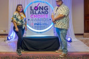 Two people stand on either side of a circular neon sign reading 'Long Island Choice Awards' at an awards display in a hotel lobby area.