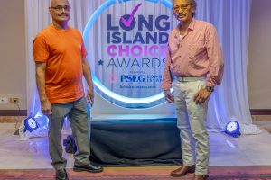 Two men pose on a stage in front of a circular neon-lit backdrop that reads 'Long Island Choice Awards'.