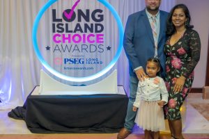 Family poses together at the Long Island Choice Awards backdrop with a blue neon circular sign behind them.