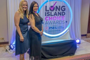 Two women in navy evening dresses pose together in front of the Long Island Choice Awards backdrop.