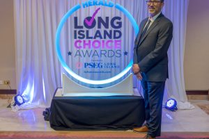 Man in a suit standing beside a circular, blue-lit Herald Long Island Choice Awards display backdrop.