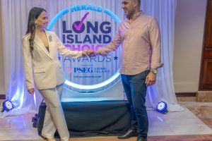Two people fist-bump on a stage in front of a circular neon-lit backdrop that reads 'Herald Long Island Choice Awards' and 'Presented by PSEG Long Island'.