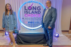 Two attendees pose beside a glowing circular Long Island Choice Awards backdrop with draped white curtains behind them, presenting a formal event scene.