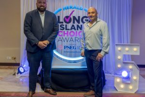 Two men pose on a stage at the Herald Long Island Choice Awards with a lit circular backdrop behind them.