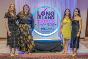 Four women in dresses pose at the Long Island Choice Awards backdrop with a glowing circular sign behind them.