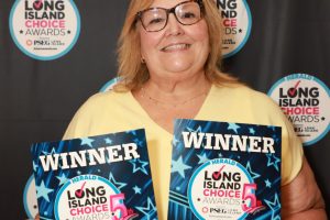 Smiling woman with glasses holding two 'WINNER' certificates for Long Island Choice Awards in front of a branded backdrop with circular logos.